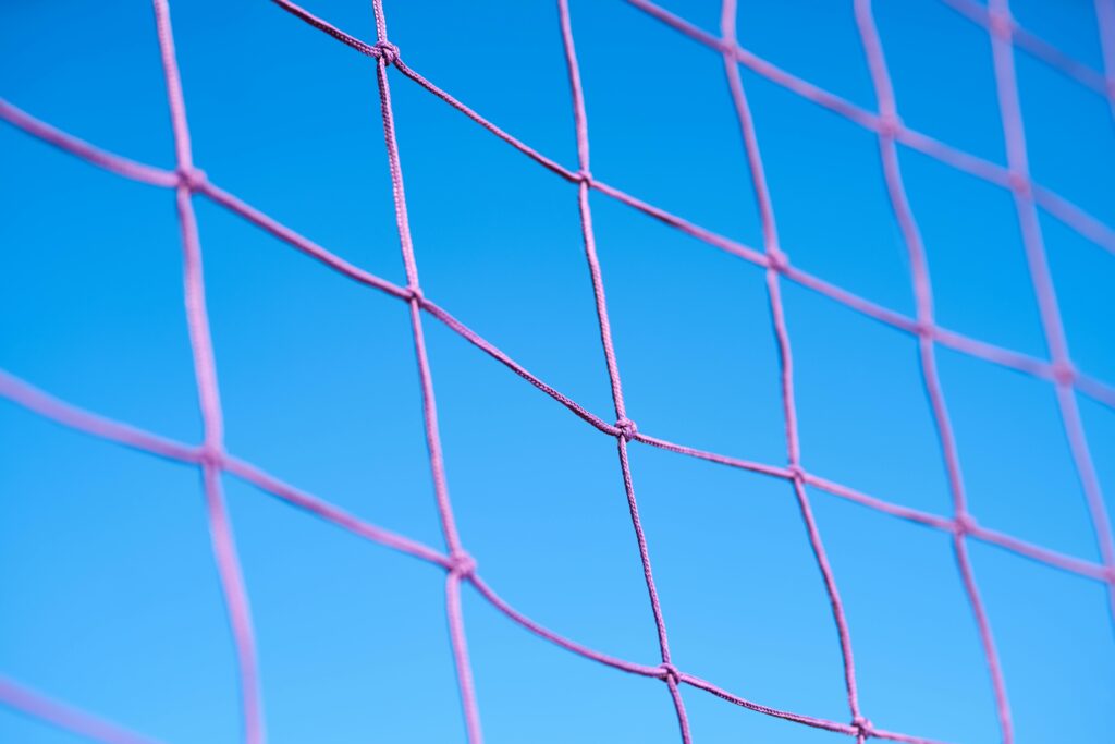 Close-up of a pink volleyball net pattern against a clear blue sky, showcasing geometric shapes.