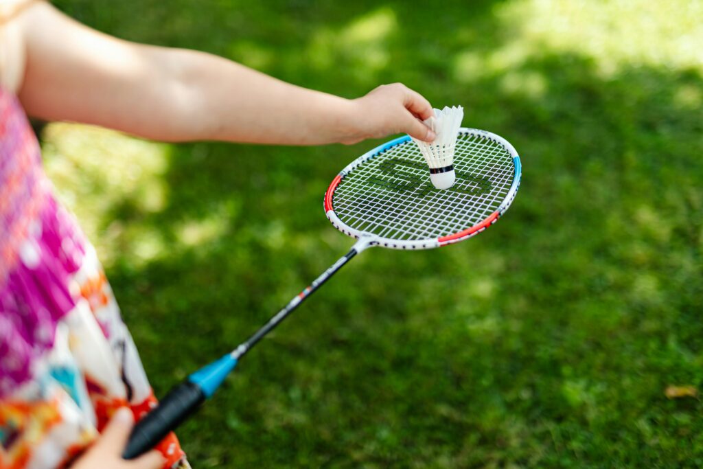 A detailed close-up of a person holding a badminton racket and shuttlecock outdoors.