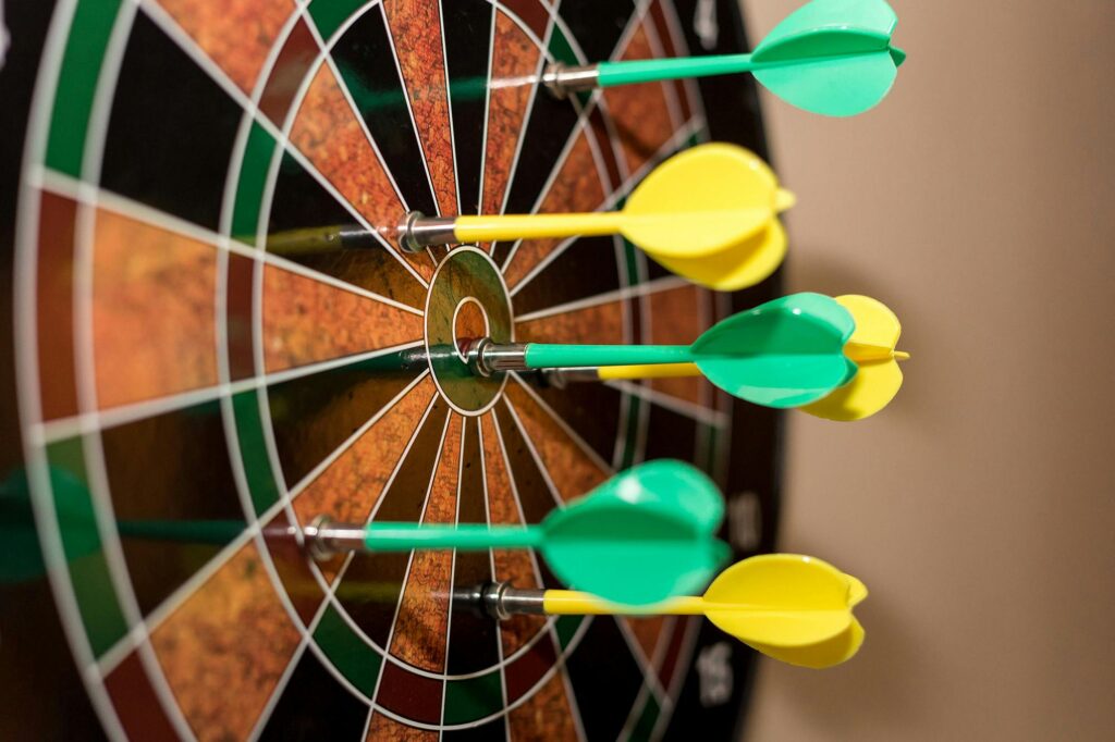 Multiple green and yellow darts precisely hitting a dartboard bullseye, indoor sport scene.