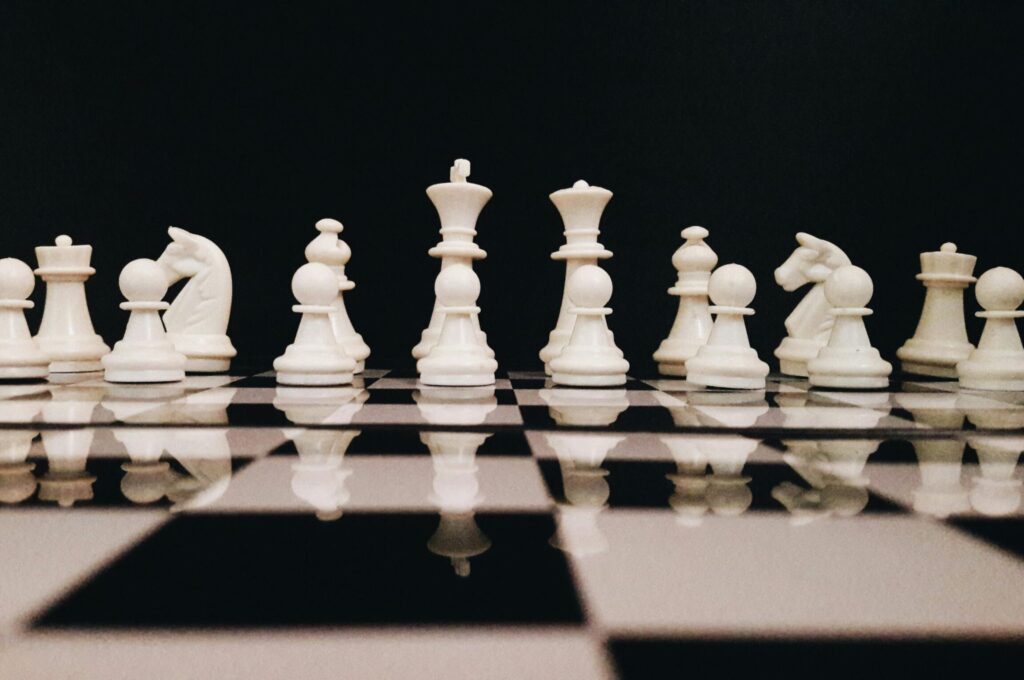 White chess pieces strategically placed on a board reflecting against a black background.